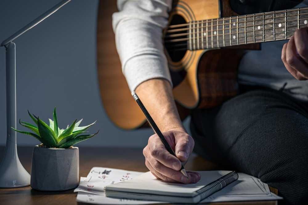 Estudiante de guitarra estudiando música con el instrumento en el regazo y tomando apuntes en un cuaderno
