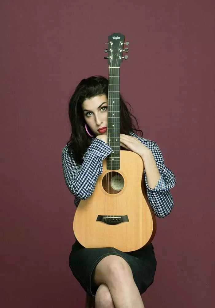 Amy Winehouse sentada con una guitarra acústica en los brazos
