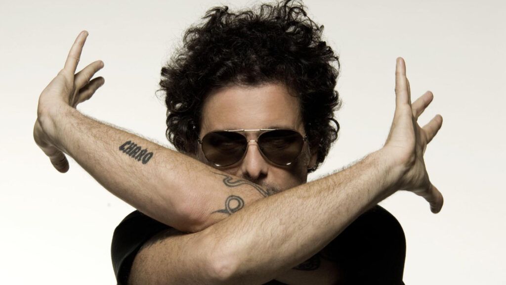 Andrés Calamaro lleva gafas de sol y posa con sus brazos y manos