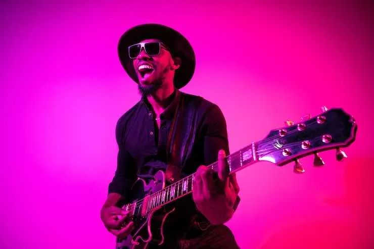 Guitarrista con sombrero negro toca la guitarra con acordes de blues en fondo color rosa
