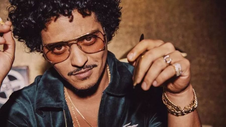 Bruno Mars lleva gafas de sol, anillos, pulseras y collares y mira a la cámara