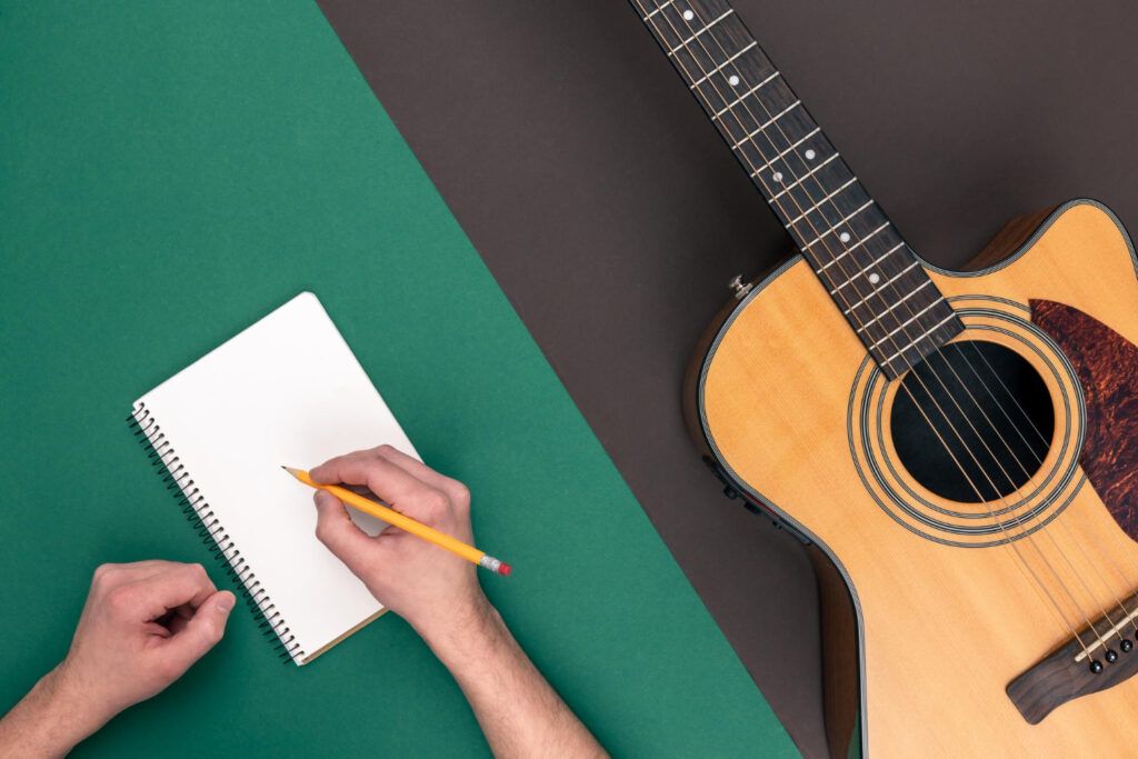 Manos escribiendo tabs y una guitarra acústica