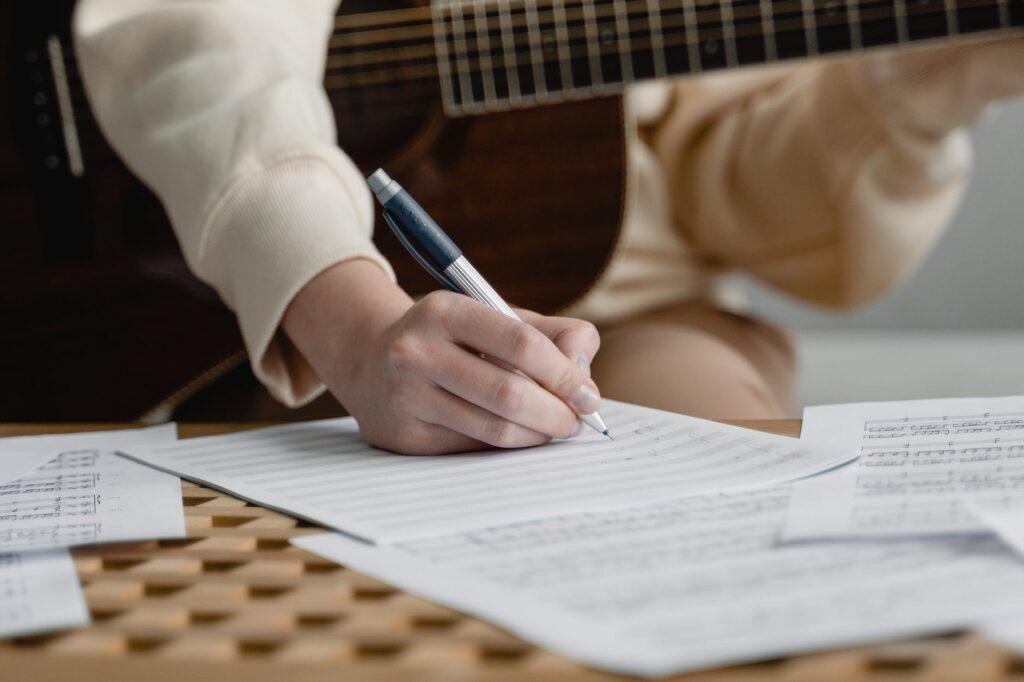 Estudante de violão com o instrumento no colo e fazendo anotações em um papel