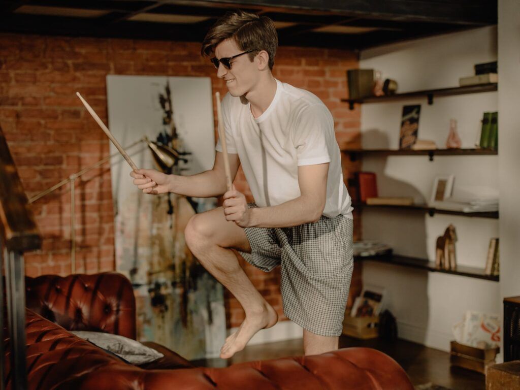 Joven haciendo un air drum para tocar batería sin hacer ruido en su sala de estar.