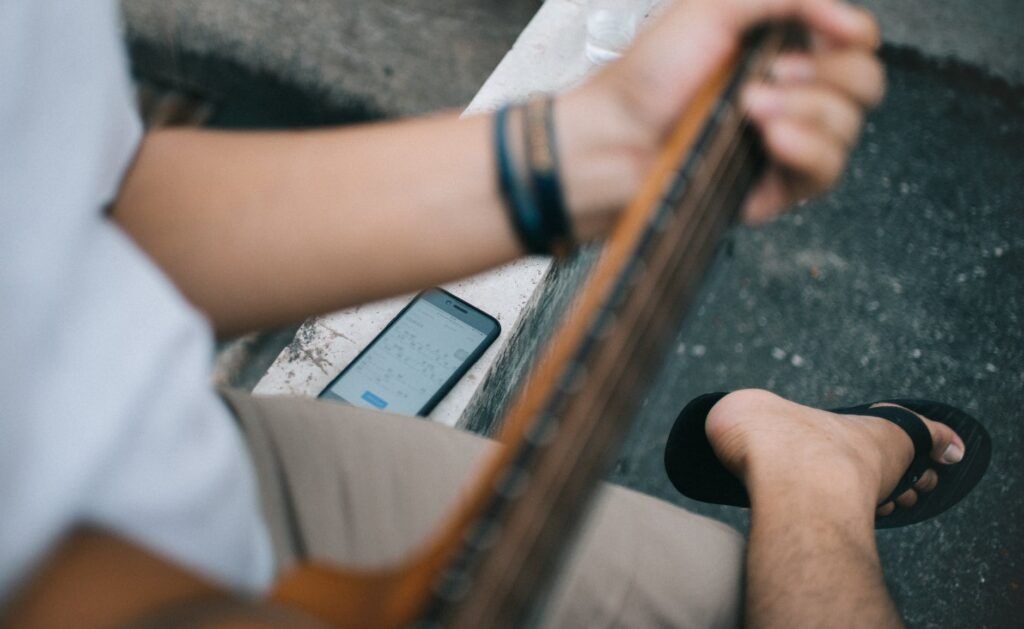 Homem toca violão e consulta um dos aplicativos de partitura no smartphone