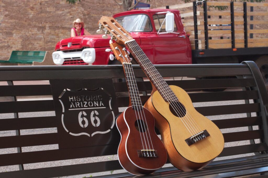 Mulher ao fundo observa um ukulele e um violão repousados num banco, ambos instrumentos são ótimos presentes de dia das mães