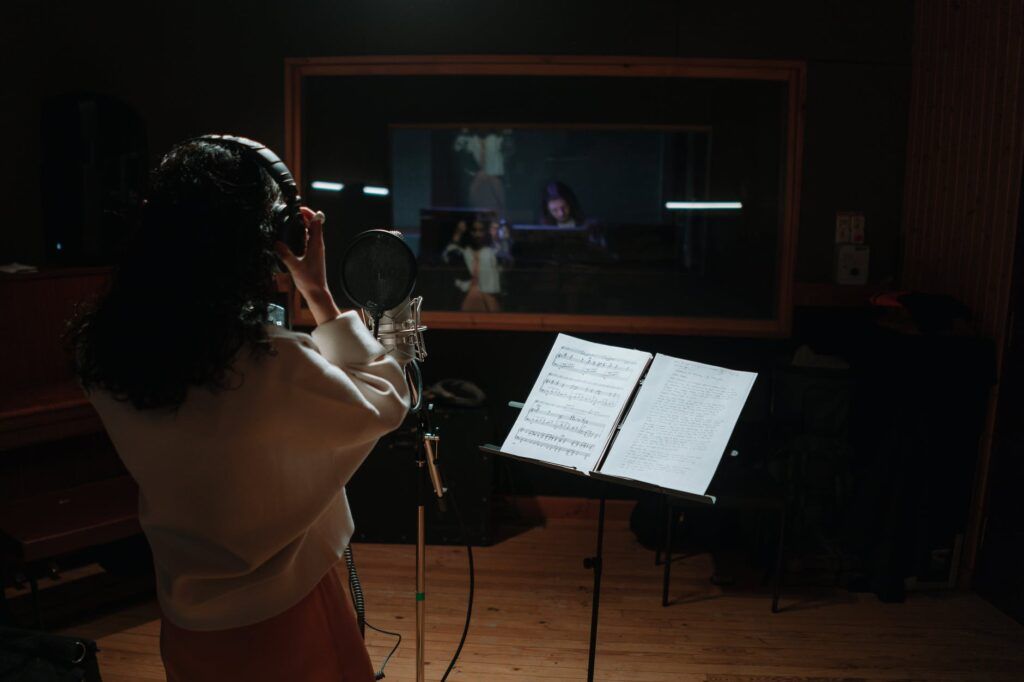 Cantora gravando voz em estudio e produtor trabalhando na mesa de som