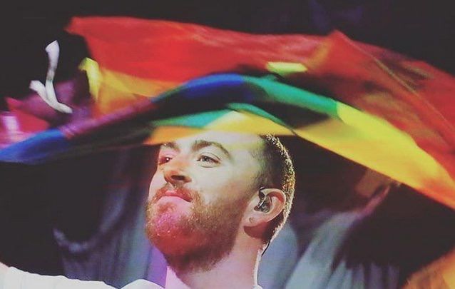 Sam Smith segurando a bandeira do arco-íris, um dos símbolos dos artistas LGBTQIA+ mais populares da atualidade