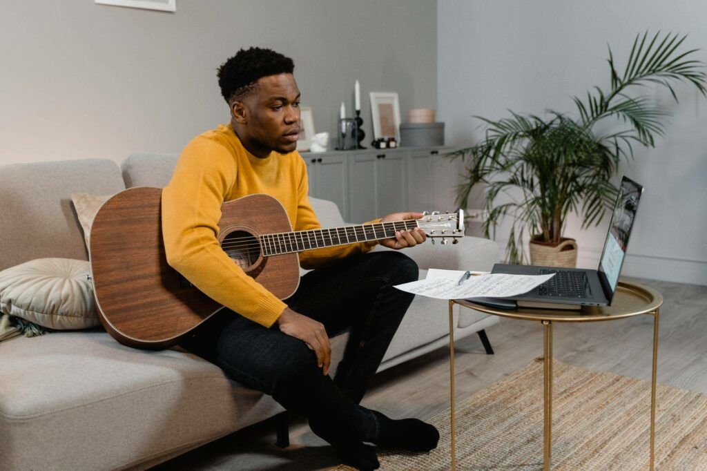 Homem negro assista aula de violão por meio de um notebook