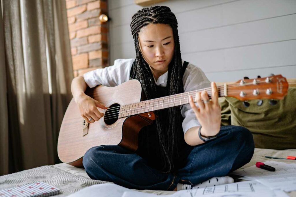 Mulher asiática sentada na cama tocando um acorde com pestana no violão