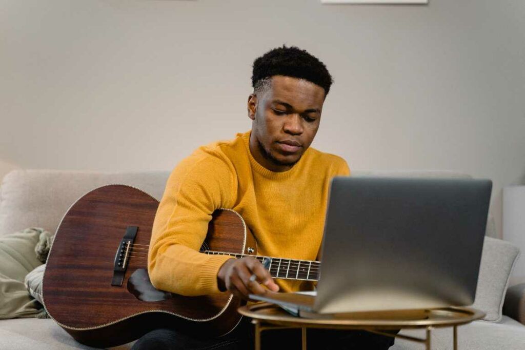 Rapaz negro usa o computador para aprender a tocar violão
