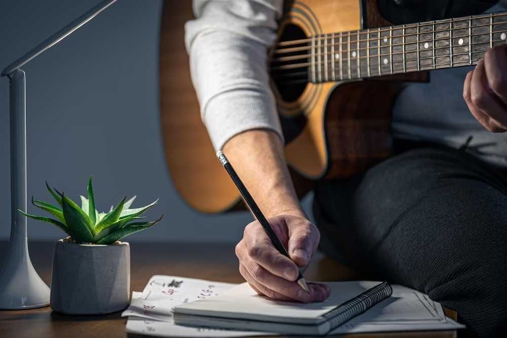 Aluno de violão estudando música com o instrumento no colo e fazendo anotações em um caderno