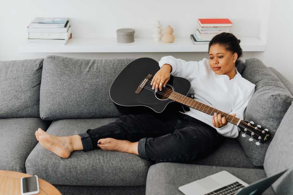 Mulher negra sentada no sofá e tocando violão com postura errada