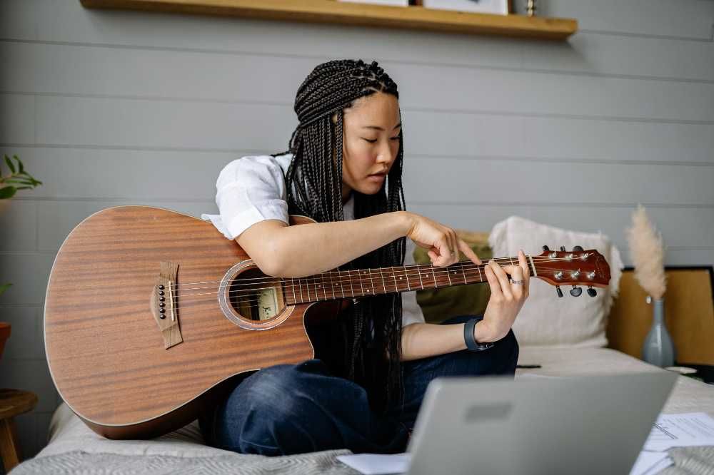 Mulher estudando formação de pestanas no violão sentada na cama