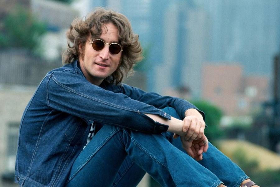 John Lennon usando jeans, óculos escuros e sentado no Central Park, em Nova Iorque