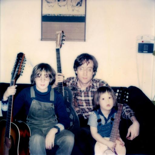 Julian Lennon, John Lennon e Sean Lennon sentados e segurando instrumentos musicais