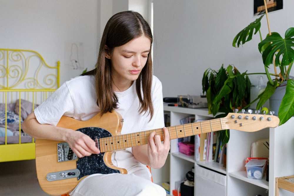 Aluna praticando guitarra em sua casa