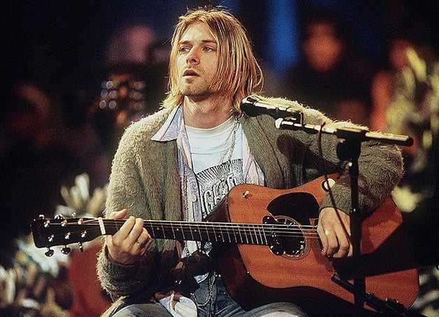 Kurt Cobain tocando violão sentado, olhando para o lado