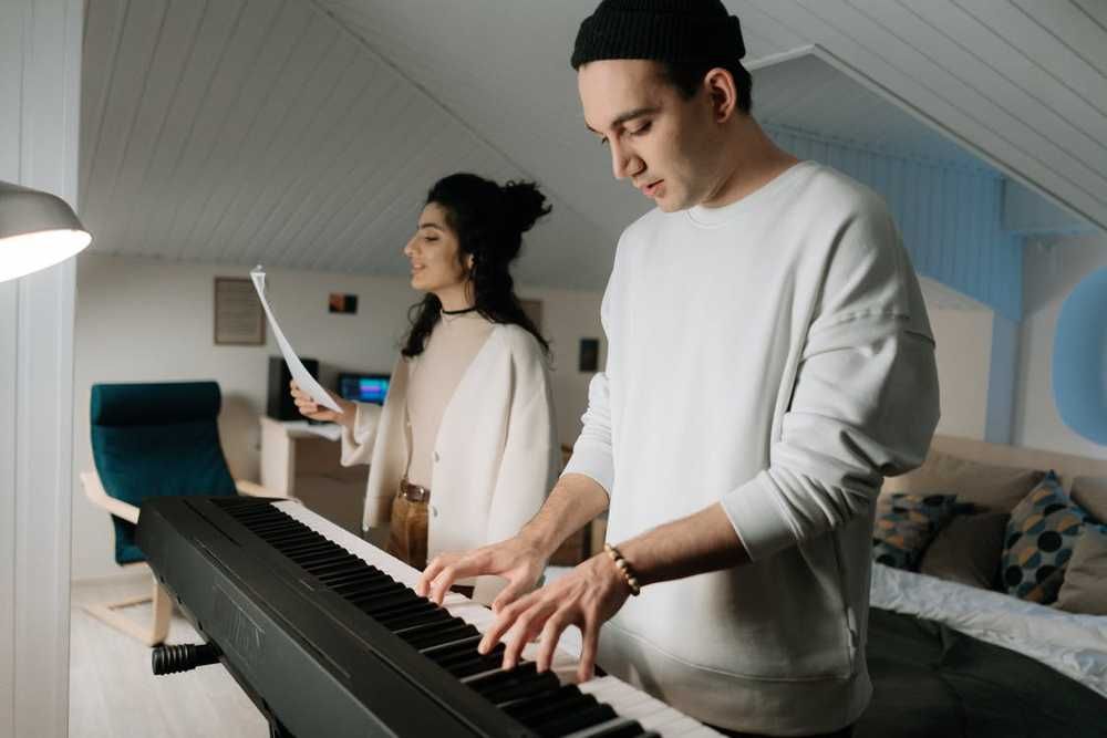 Homem tocando piano digital e mulher cantando no estudo de melodia