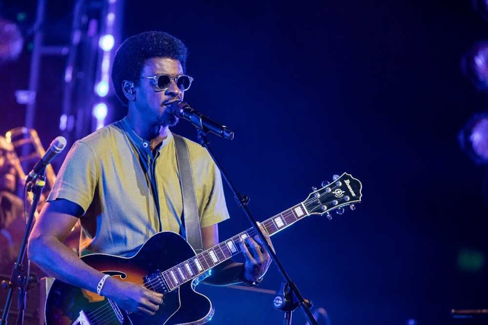 Seu Jorge de óculos escuros cantando e tocando guitarra em show