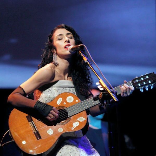 Marisa Monte tocando violão e cantando de olhos fechados em show