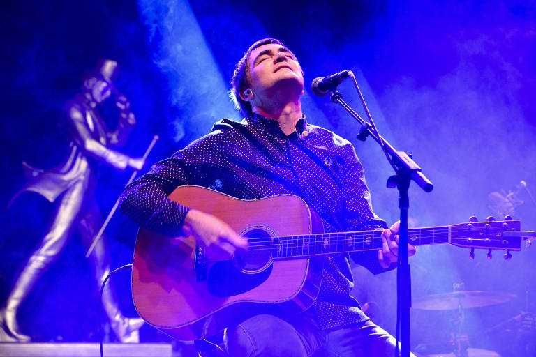 Samuel Rosa em show do Skank tocando violão sentado e com a cabeça virada para cima de olhos fechados