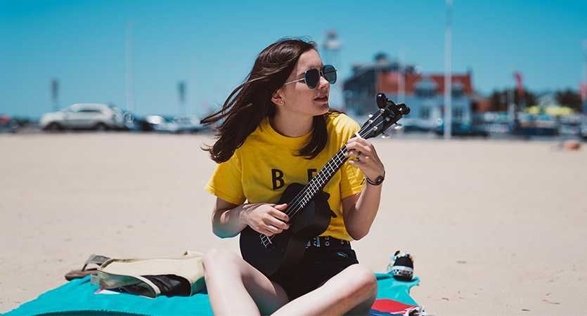 Jovem tocando ukulele na praia se óculos escuros
