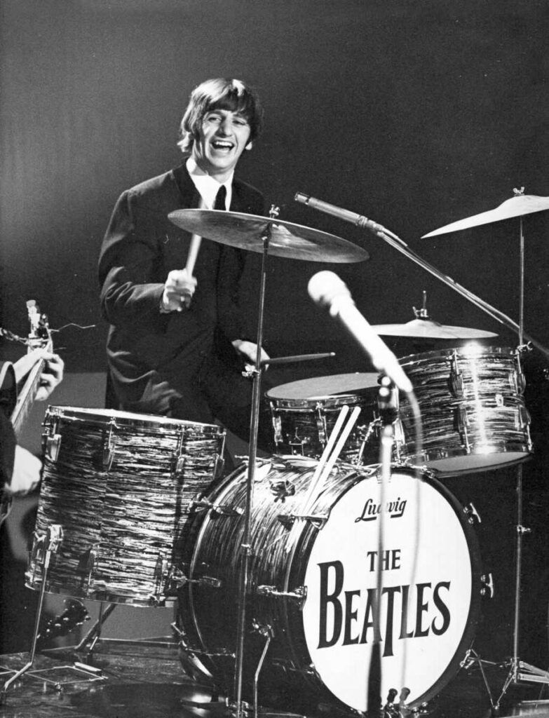 Ringo Starr tocando bateria sorrindo em show dos Beatles