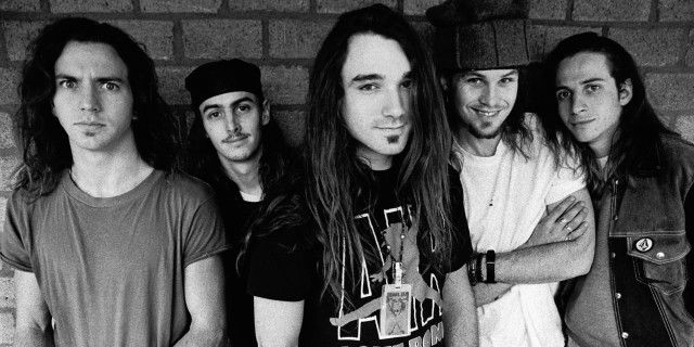 Integrantes do Pearl Jam posando para foto em preto e branco com um muro de tijolos ao fundo