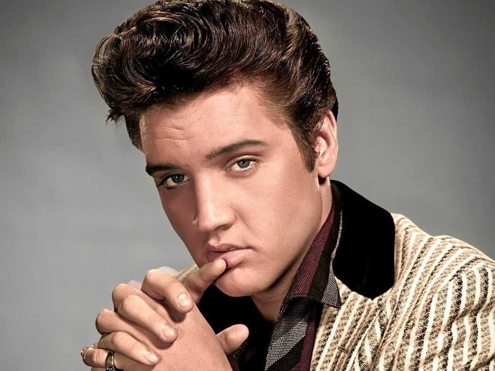 Elvis Presley em sessão de fotos olhando de forma seuduzente para a câmera com as mãos cruzadas encostando no rosto