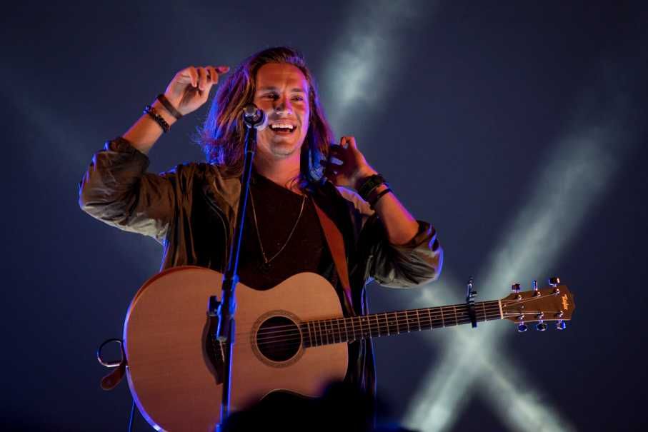 Vitor Kley em show com violão sorrindo mexendo no cabelo