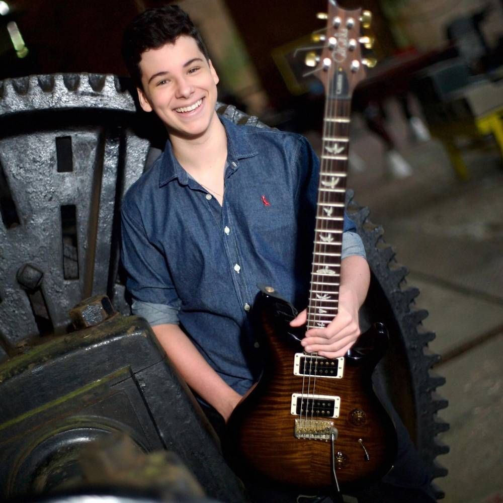 Daniel Fonseca segurando e guitarra e sorrindo para foto em cenário mecânico