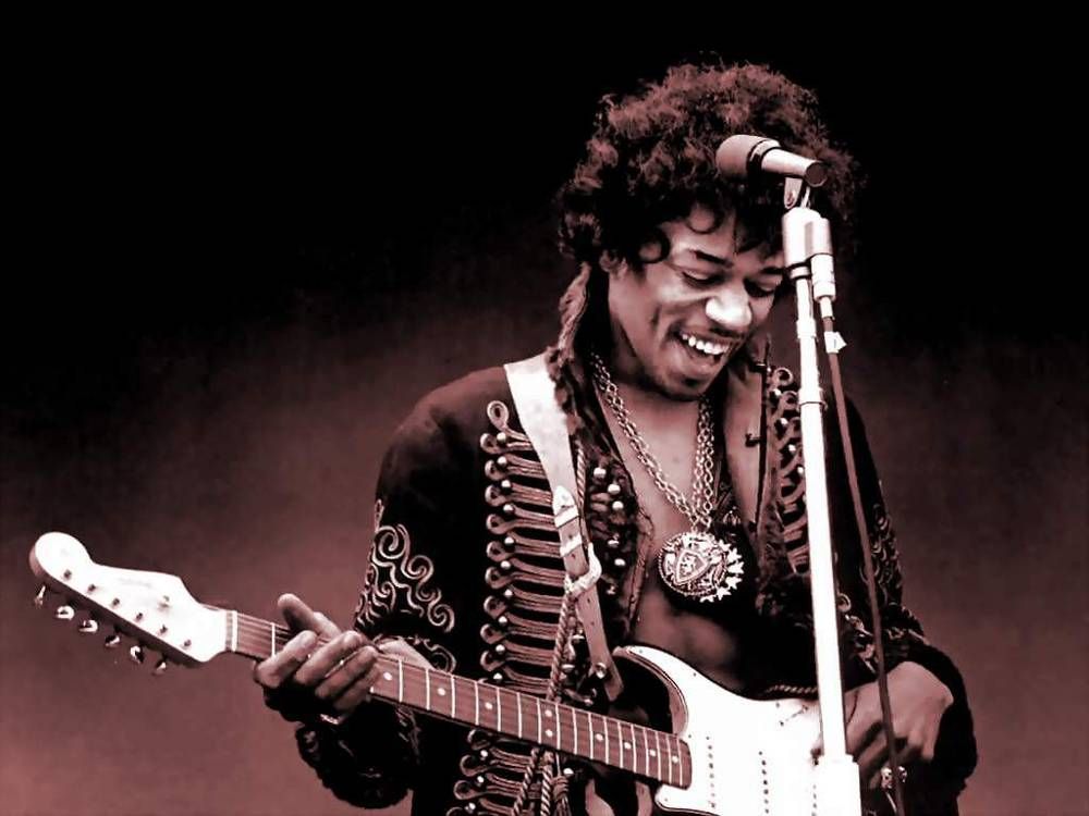 Jimi Hendrix tocando guitarra em show sorrindo