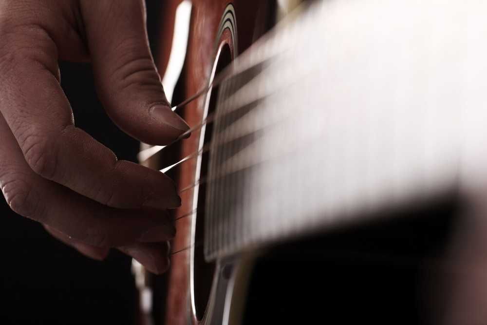 Dedos de um músico dedilhando as cordas de um violão