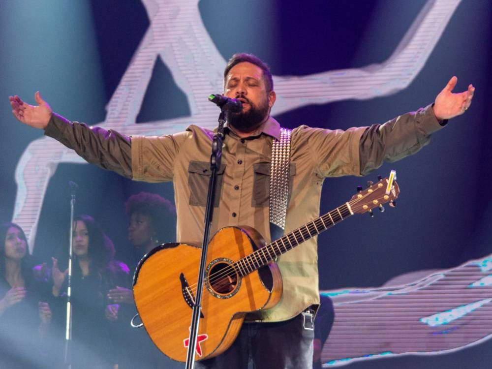 Cantor Fernandinho com violão em show com os braços estendidos para o alto