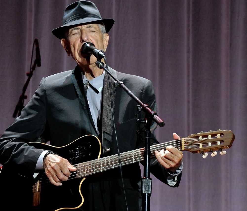 Leonard Cohen tocando violão e cantando de olhos fechados em show