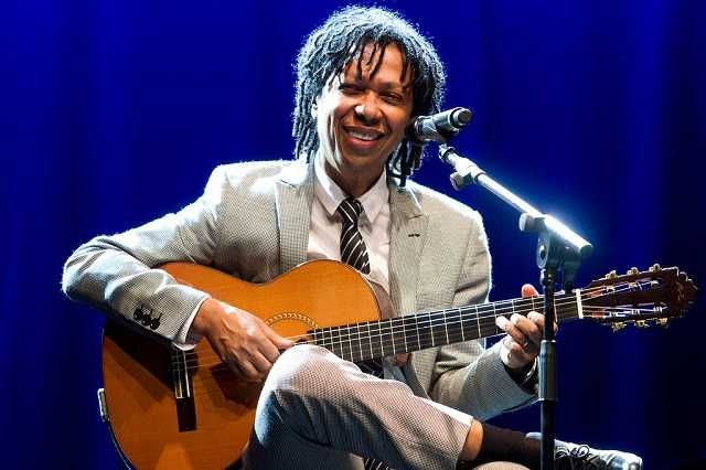 Djavan tocando violão sorrindo em show