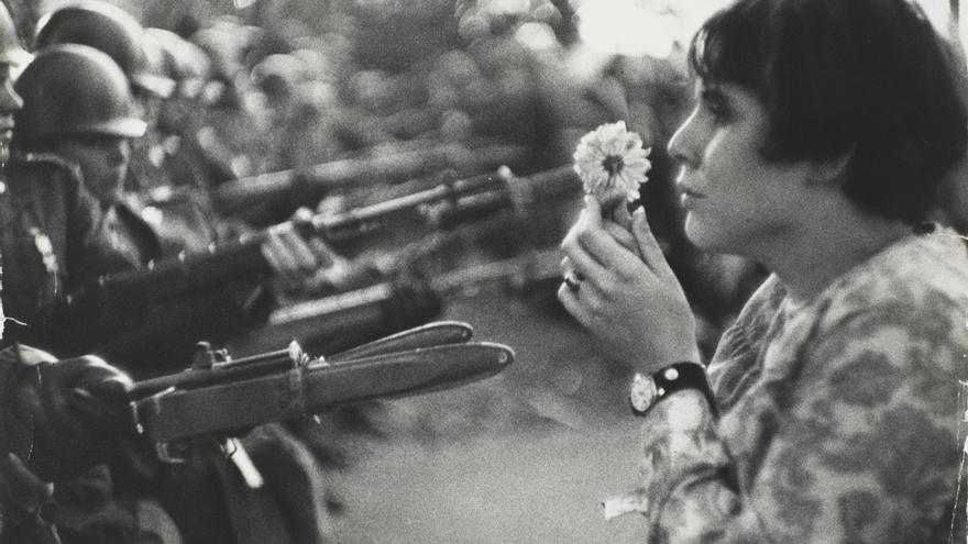 Jovem ativista mostrando uma flor para militares armados