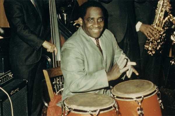 O percussionista Mongo Santamaría tocando uma dupla de congas sorrindo