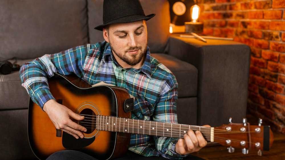 Homem tocando blues no violão sentado e com chapéu preto