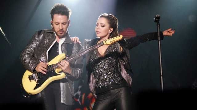 Junior, tocando guitarra, e Sandy, olhando para o irmão, em show