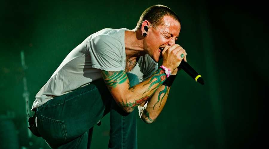 O vocalista Chester Bennington cantando com as duas mãos no microfone e de olhos fechados em show do Linkin Park