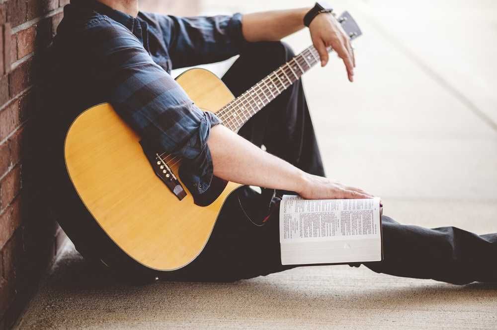 Aluno de violão sentado no chão com o instrumento no colo e uma bíblia apoiada na perna