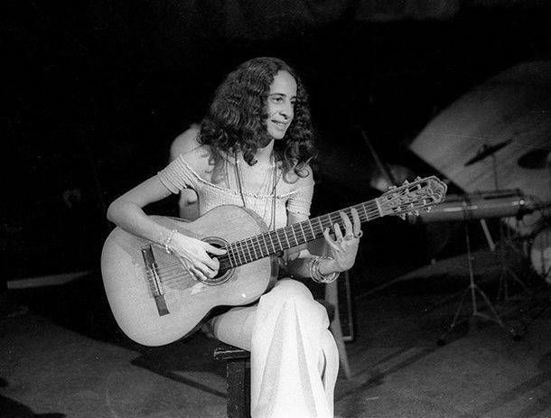 Maria Bethânia tocando violão sentada