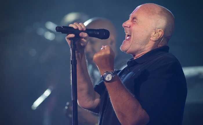 Phil Collins cantando em show segurando o microfone com uma mão