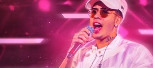 Cantor Kevinho canta com um microfone em sua mão no centro da imagem