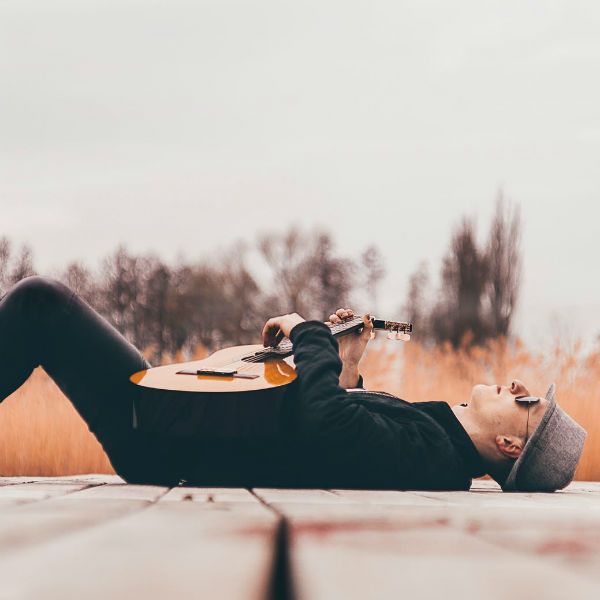 Homem deitado, relaxando, e dedilhando um violão
