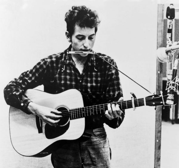 Bob Dylan tocando guitarra y armónica al mismo tiempo