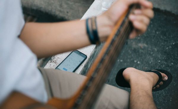 Guitarrista tocando su instrumento mientras mira una aplicación para músicos en su celular
