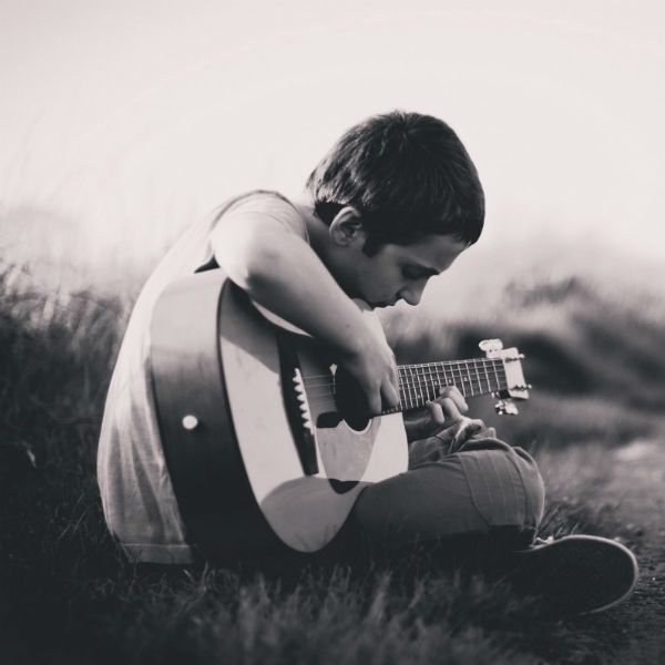 Sentado na grama, menino toca violão de nylon